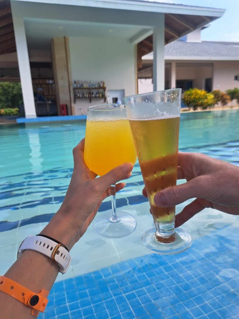 Two hands doing a cheers with a beer and orange drink in a pool