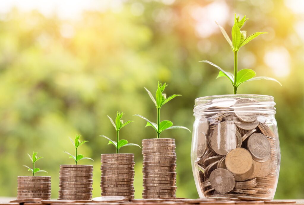 Piles of coins and a jar of coins with plants sprouting from them