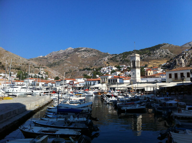 Boats in the harbour or port of the Greek Island Hydra with the town and mountains in the background and bright blue sky