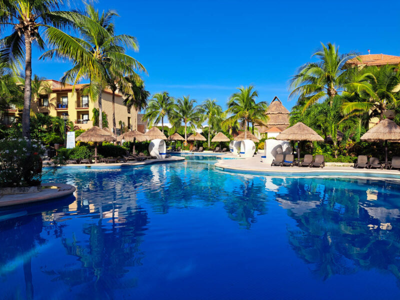 Quiet all-inclusive resort pool with palm trees and hotel buildings in the background