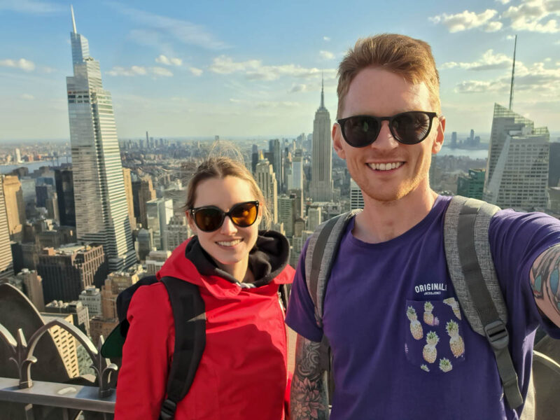 A man and a woman standing on top of a building in New York, with the Empire State building in the background