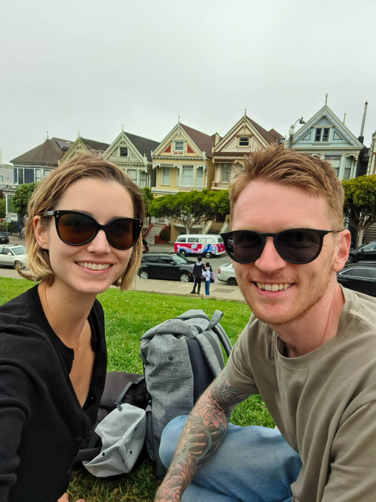 A couple sat in Alamo Park with the Painted Ladies behind them