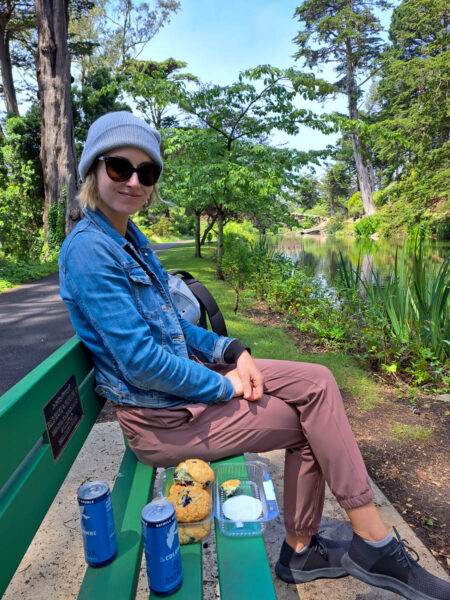 A woman sitting on a bench in Golden Gate Park with picnic food.