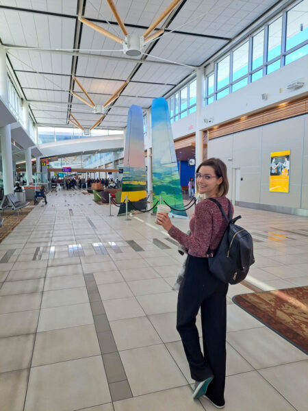 A woman smiling and looking back at the camera as she walks in an airport holding a coffee