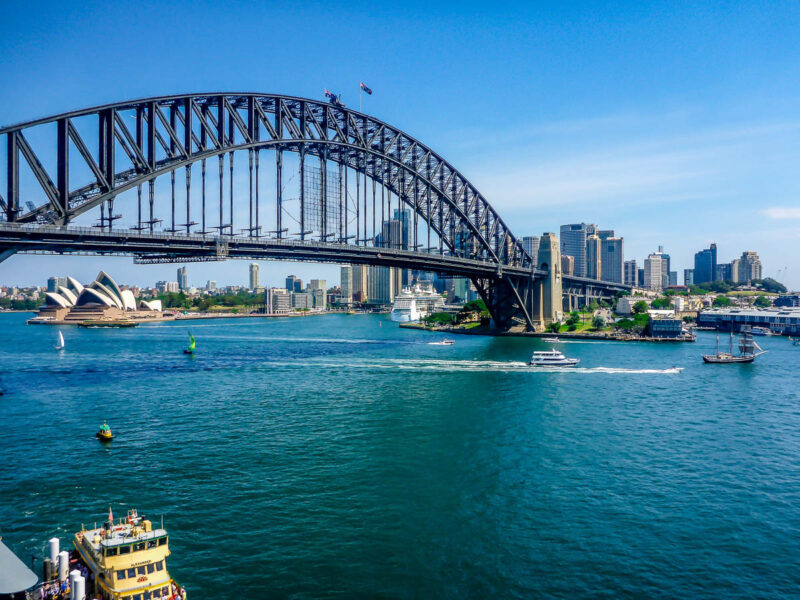 Sydney Harbour Bridge over Sydney Harbour with the Sydney Opera House in the background, blue water and bright blue sky