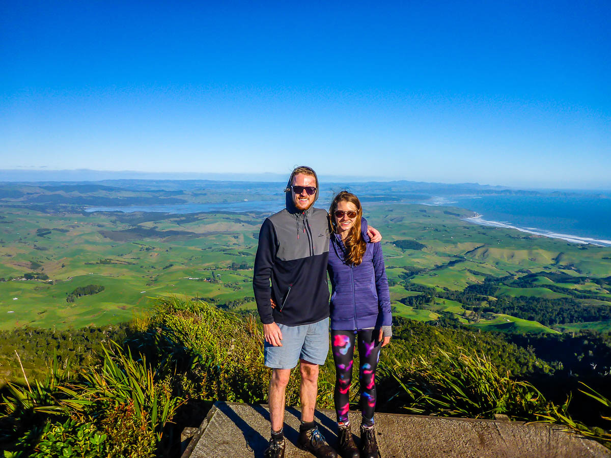 A man and woman on a mountain in New Zealand with rolling green scenery behind them