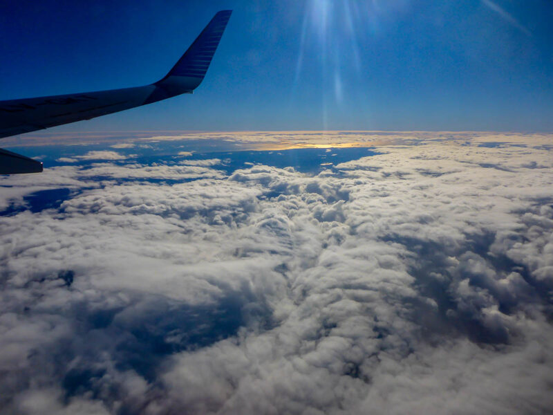 View from an airplane window of blue skies, clouds below and the airplane wing