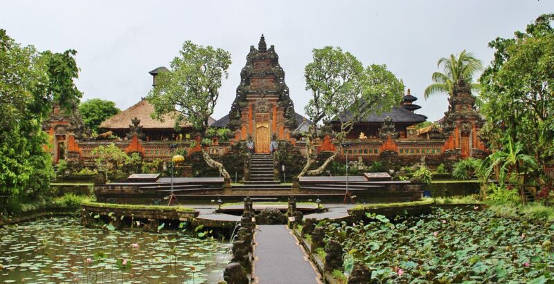 A path leading to a temple in Ubud, Bali, Indonesia with lily-pad filled ponds on either sides and lush greenery around the temple