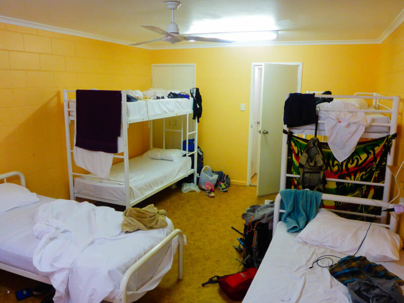 Messy dorm room in a hostel with 2 bunk beds, 2 single beds, and clothing sprawled out everywhere