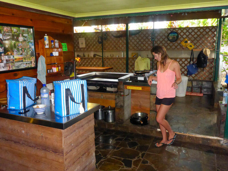 A woman standing in a budget-friendly shared kitchen in a hostel in rustic Atherton Tablelands, Australia.