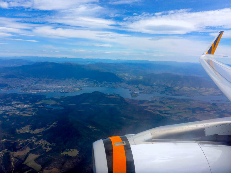 View outside the window of a plane with part of the plane, a city, lake and mountains in the background