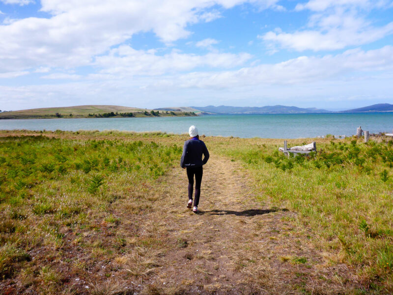 A woman walking on a trail headed towards a lake in Australia, budget travel friendly form of transportation