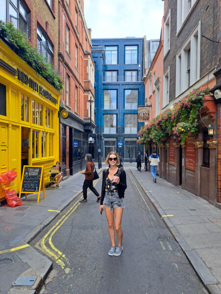 A woman standing in a narrow street in London, England with colorful old buildings around her