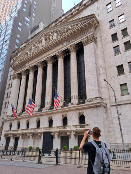 A man taking a photo in front of Wall Street in New York City