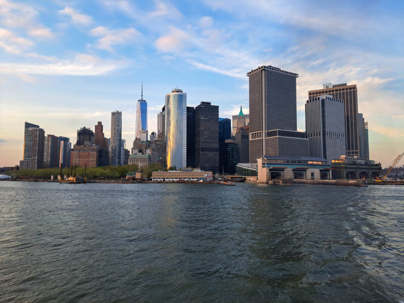 A view of New York City and the financial district from the Staten Island ferry with skyscapers in the background, water, blue sky and clouds