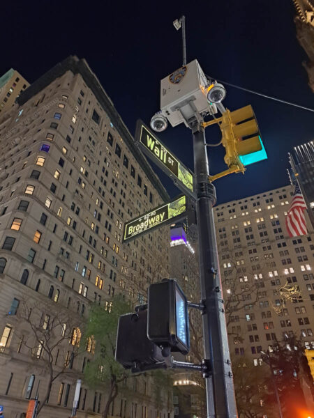 Tall skyscraper buildings, traffic lights and the street signs for the corner of Wall Street and Broadway in New York City, as seen from the ground looking up