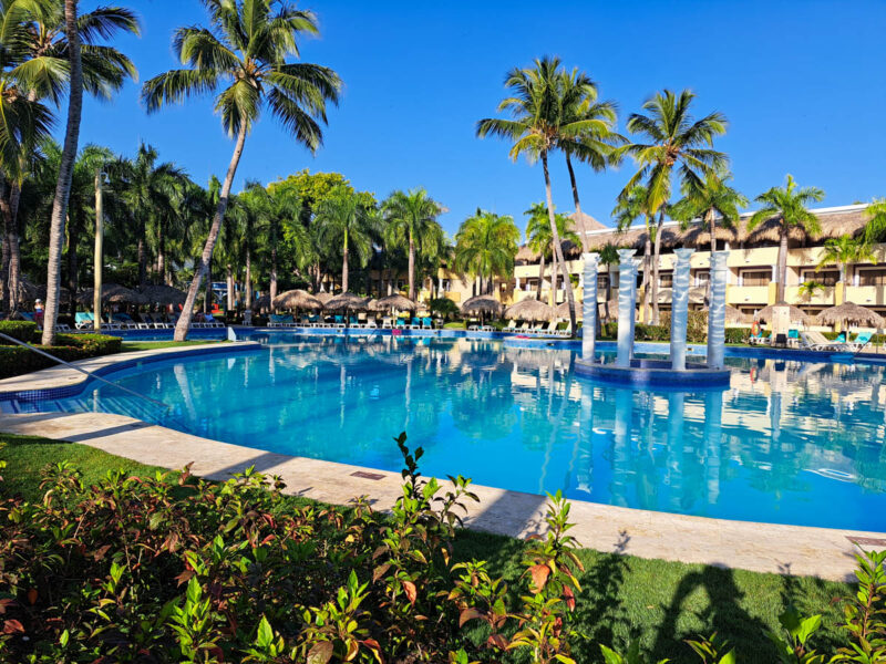 Tropical hotel pool with palm trees and shrubbery around, the resort rooms in the background, and deep blue sky