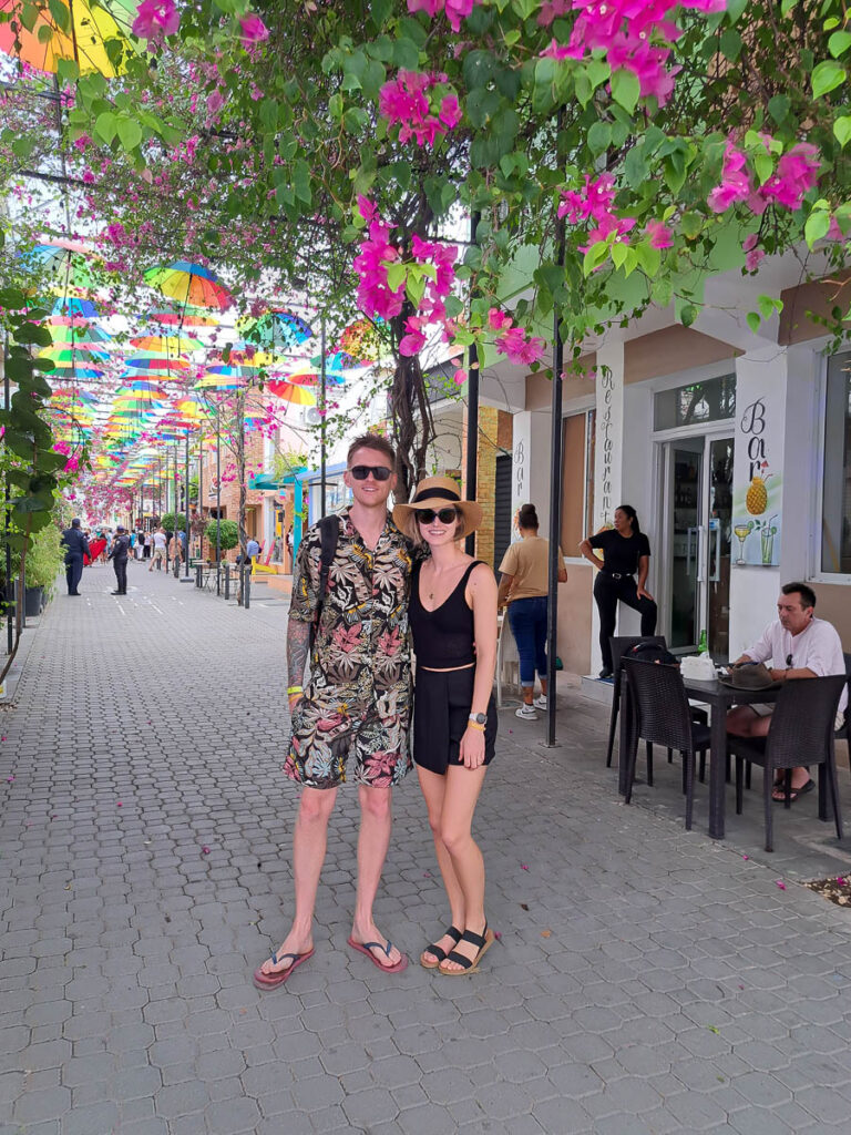 A man and women dressed in all-inclusive resort vacation fashion standing in the colorful Umbrella Street in Puerto Plata, Dominican Republic