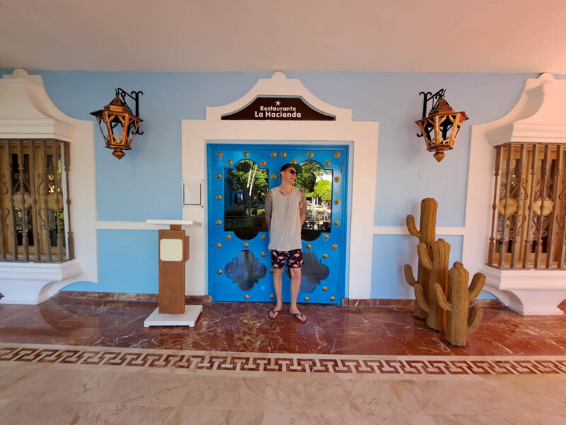 A man laughing and enjoying himself outside of a themed Mexican restaurant with cacti plants to his left, giant lanterns on either side, and a beautifully adorned blue door