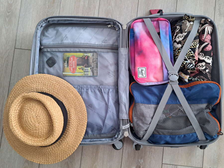 A small suitcase lying open packed with clothes, a wash bag and a beach hat