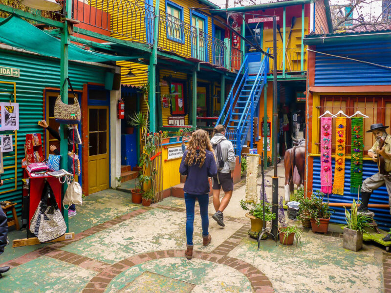 A woman and man walking towards shops in the colorful neighborhood of La Boca in Buenos Aires, Argentina.