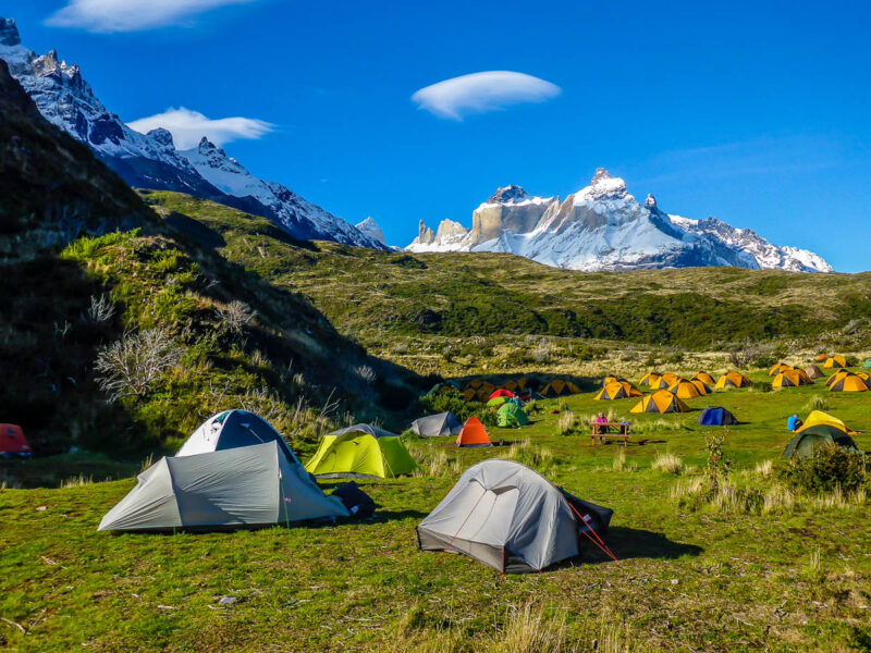 Picturesque campsite in Torres del Paine National Park, Chile. Snow capped mountains in the background with lush green grass covered hills closer to the campsite and colorful tents. A budget friendly way to travel.