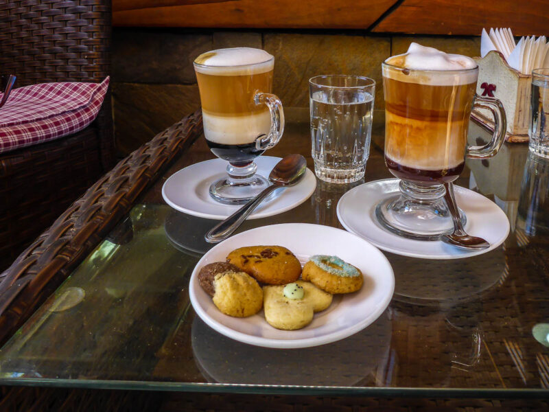 A table with a plate of 4 cookies and 2 lattes sitting on top.