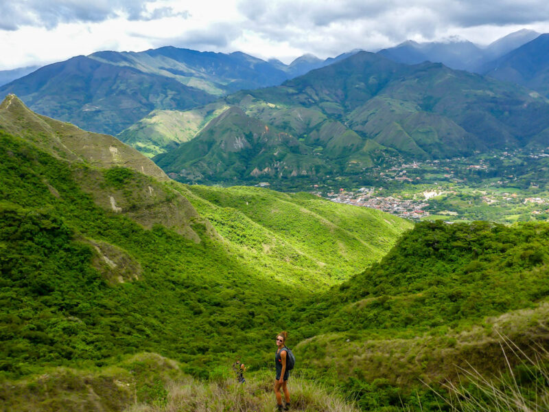 A woman hiking near Vilcabamba, Ecuador with rolling hills and mountains covered in lush greenery and the small village in the background.