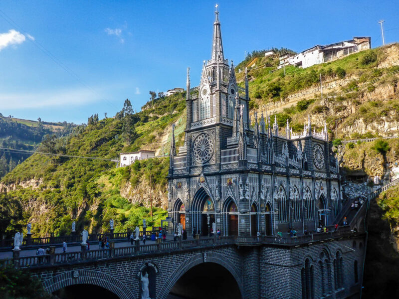 Stunning gothic style cathedral tucked against a mountainside in Colombia near the city of Ipiales. The hillside is green with trees and plants.