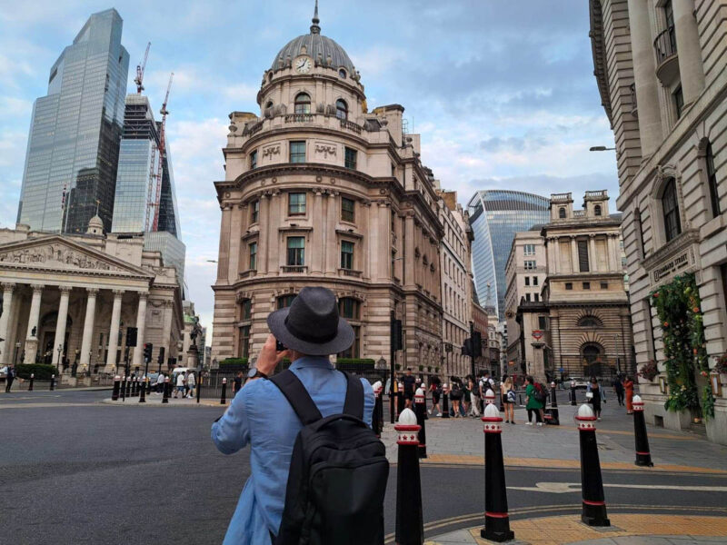 A man wearing a black hat taking a photo of the Bank of England in London