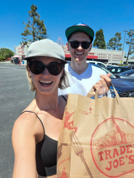 A woman and man smiling at the camera with their Trader Joe's shopping bag on a visit San Mateo