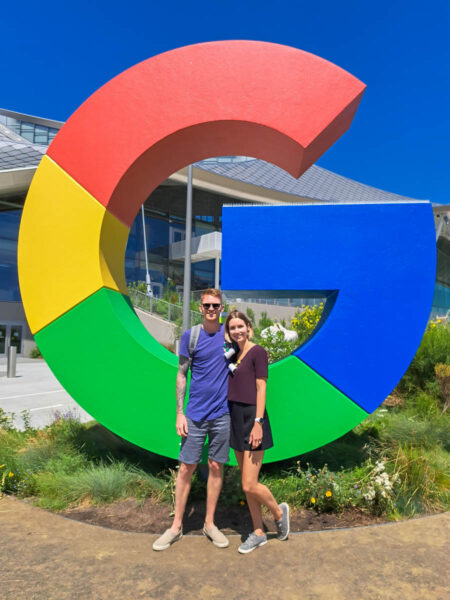 A man and woman posing and smiling in front of a giant red, yellow, green, and blue colored "G" for Googleplex in California.