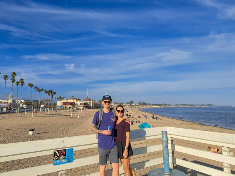 A man and woman posing on a wharf overlooking the beach and water at Santa Cruz