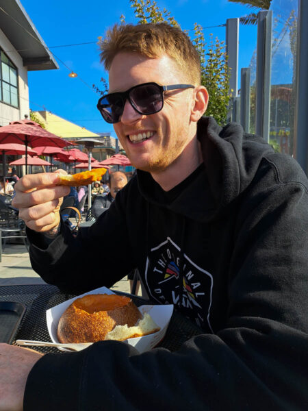 A man smiling and enjoying a sourdough soup bread bowl at Boudin Bakery in San Francisco