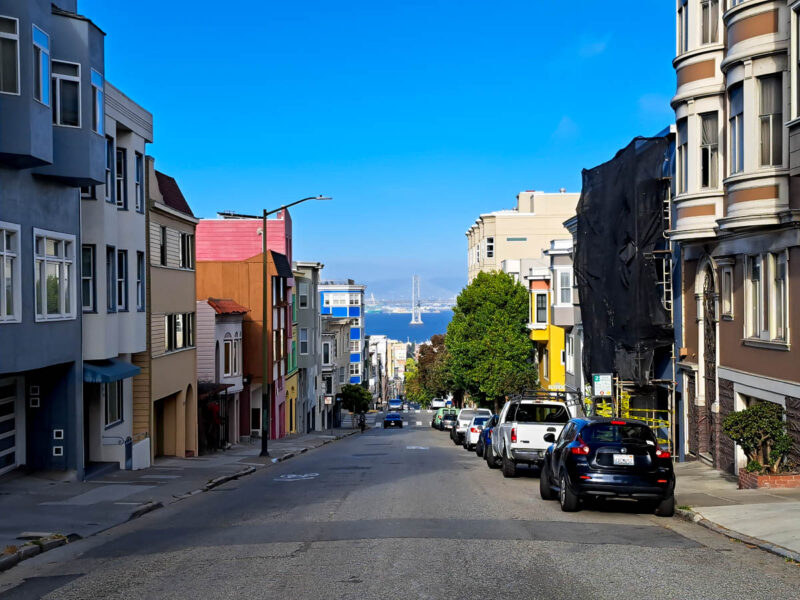 San Francisco street with colorful houses and buildings on either side and the San Francisco Bay and bridge in the background