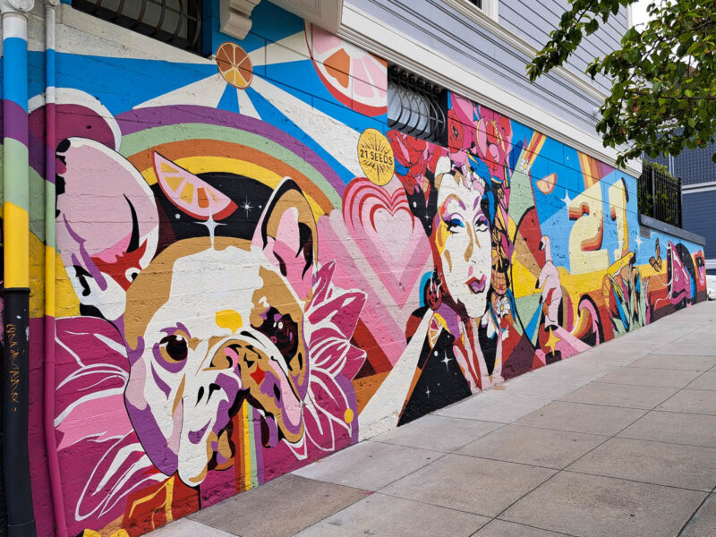 Colorful mural on the side of a building with tones of pinks and blue, a painting of a dog and woman