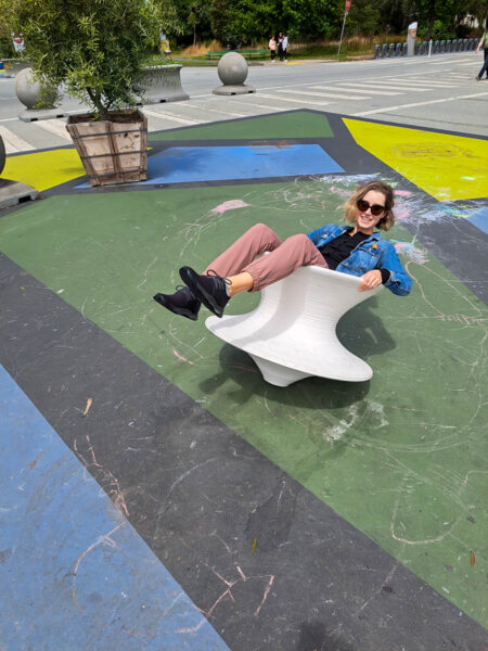 A woman leaning back in a wobbly spinning top chair on brightly colored pavement