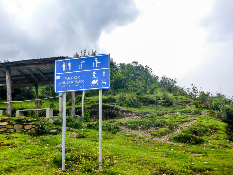 A big blue sign denoting washroom and water facilities on the trail to Machu Picchu. There is a covered hut with benches and a table.