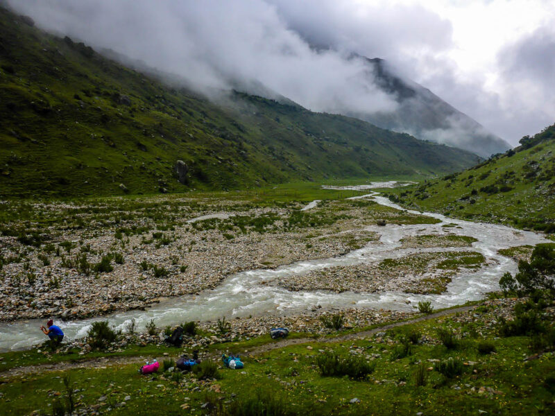 A man kneeling beside small fast flowing streams in the valley between tall mountains