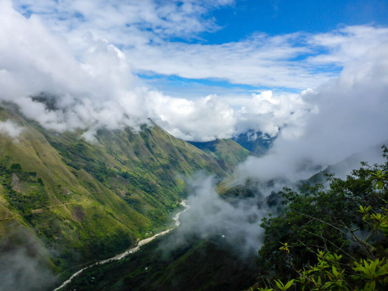 View of a path down in a ravine with tall mountaons on either side, blue sky and clouds.