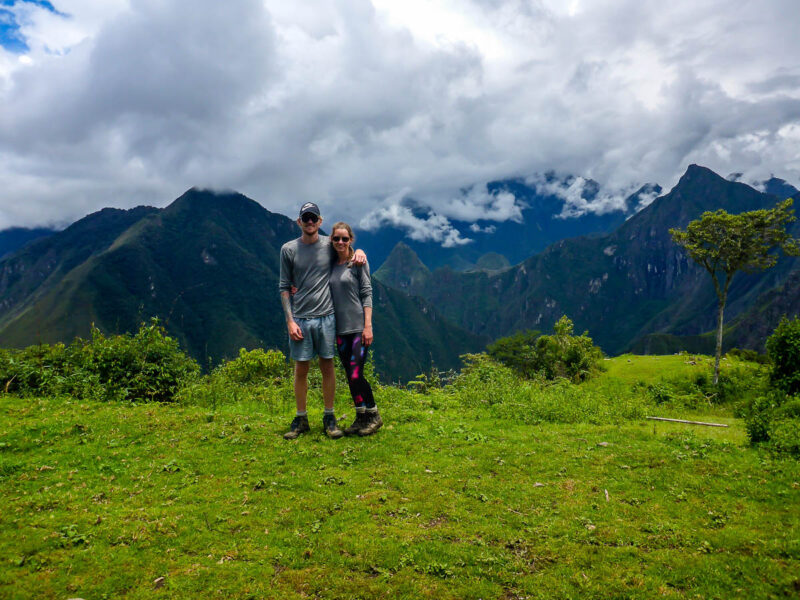 A man and women posing on a mountain with views of taller mountains and Machu Picchu in the background.