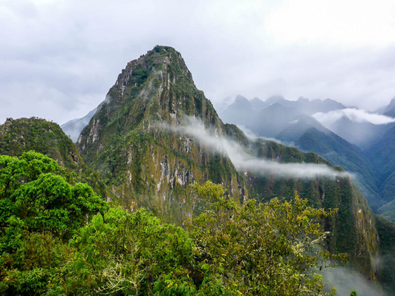 A tall mountain in the middle of the Peruvian Jungle surrounded by lush greenery and clouds.