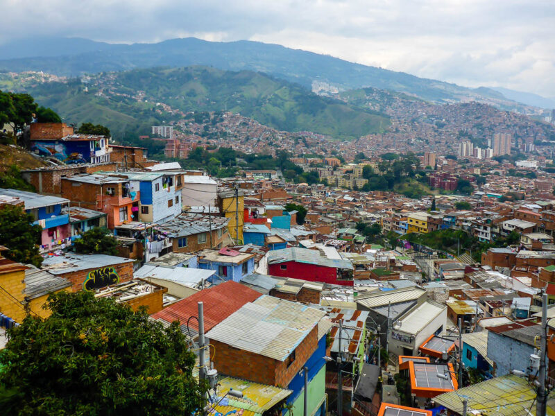 Hillside view of houses and colorful buildings in Medellín, Colombia with mountains in the background.