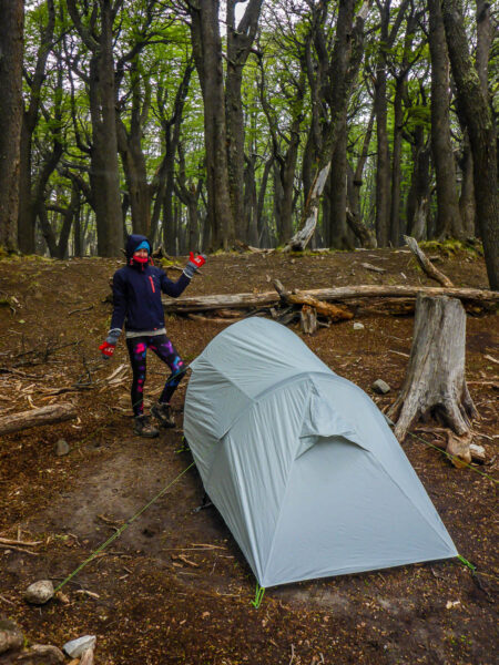 A woman posing next to her tent in the woods