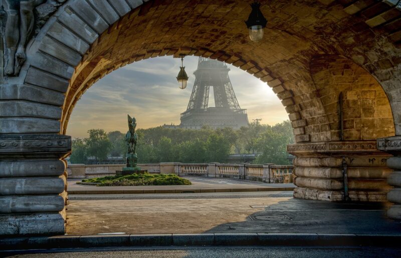 A view of the Eiffel Tower at sunrise through a stone archway in Paris, France