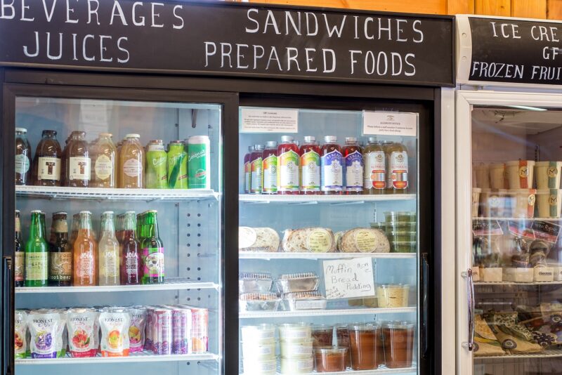 Three grocery fridges beside each other. One with beverages, another with sandwiches and prepared foods, and the other with ice cream.