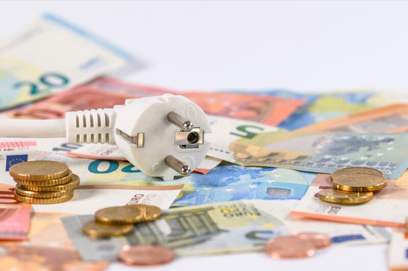 Euro bank notes and coins with a white travel adapter on top