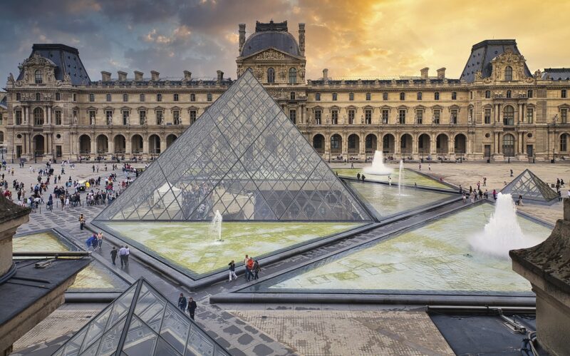 Louvre museum and famous louvre pyramid with people walking around.