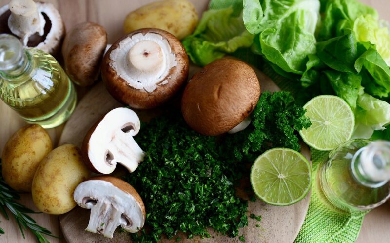 Mushrooms, chopped parsley, sliced limes, potatoes, lettuce, and olive oil on a cutting board