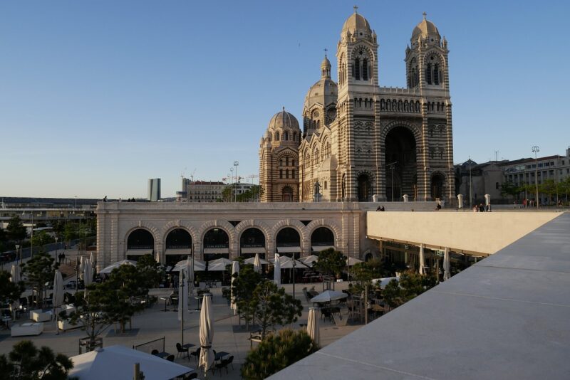 Cathédrale de La Major in Marseille, France from a distance during sunrise showing footpaths and bridges, restaurant patio set ups, and people walking around.